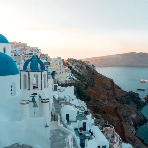 urlaub buchen. Blick auf die weißen Häuser und blauen Kuppeln von Santorini bei Sonnenuntergang mit Blick aufs Meer
