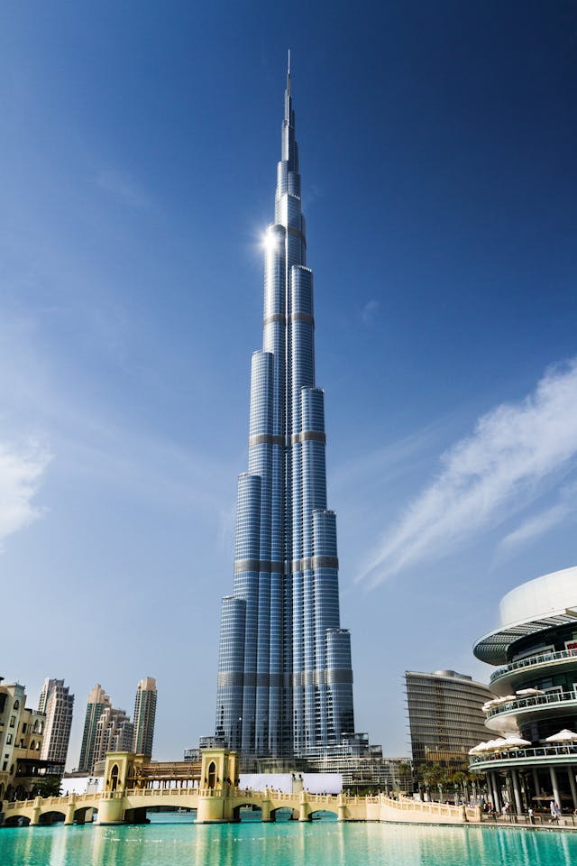 Dubai Urlaub. Burj Khalifa vor klarem Himmel mit umliegender Skyline und Wasserfläche – Symbol für moderne Architektur und Luxusurlaub in Dubai.