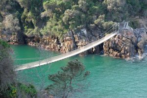 Hängebrücke über türkisfarbenem Wasser zwischen Felsen und grüner Vegetation – Namibia Rundreise mit Natur- und Kulturerlebnissen