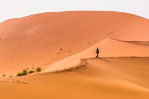 Person auf orangefarbenen Sanddünen unter blauem Himmel – Wüstenlandschaft in Namibia erleben