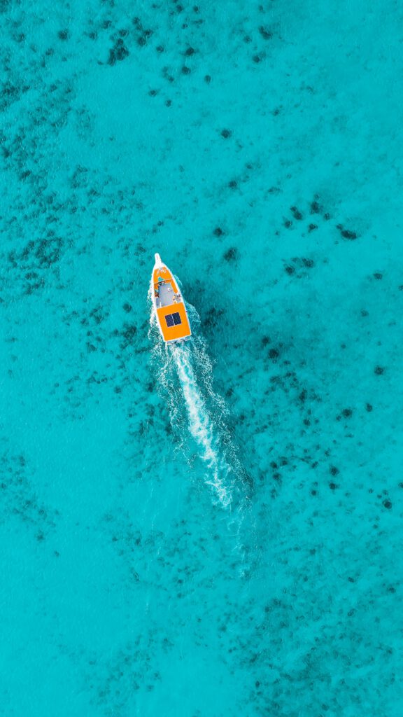 Urlaub Dominikanische Republik. Orangefarbenes Boot fährt durch türkisblaues Wasser mit Korallenstrukturen – Sinnbild für Abenteuer und Naturerlebnisse in der Dominikanischen Republik.