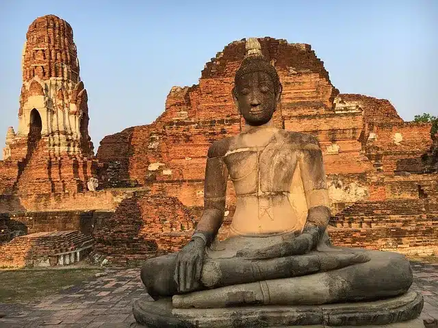 Thailand Rundreise. Große Buddha-Statue vor antiken Backsteinruinen in Ayutthaya, Thailand – Symbol für historische und spirituelle Reiseziele abseits der Touristenpfade.