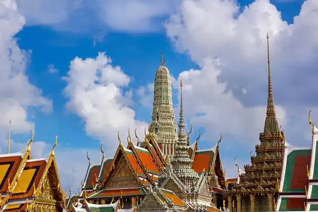 Thailand Urlaub. Prunkvolle Tempel in Bangkok mit goldenen Spitztürmen und kunstvollen Fassaden vor blauem Himmel – typisch für Thailands kulturelles Erbe.