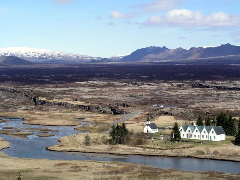 Kirche mit grünem Dach am Flussufer im Thingvellir Nationalpark mit schneebedeckten Bergen im Hintergrund