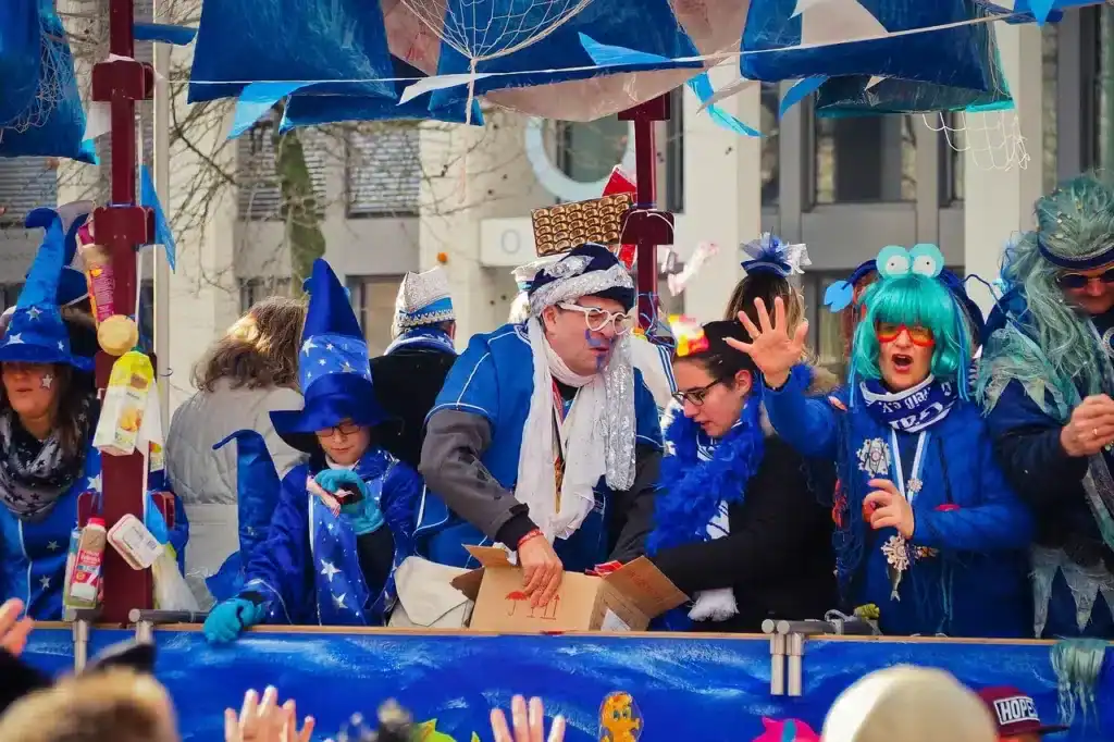 Rosenmontagsumzug in Köln mit bunt verkleideten Menschen auf einem Festwagen beim Kamellewerfen