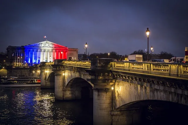 Last Minute Urlaub Frankreich. Pont de la Concorde und Palais Bourbon in Paris bei Nacht, beleuchtet in Blau, Weiß und Rot