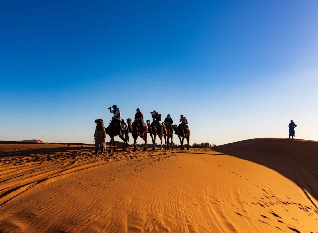 Menschen reiten auf Kamelen über Sanddünen bei Sonnenuntergang – Abenteuertour in der tunesischen Sahara
