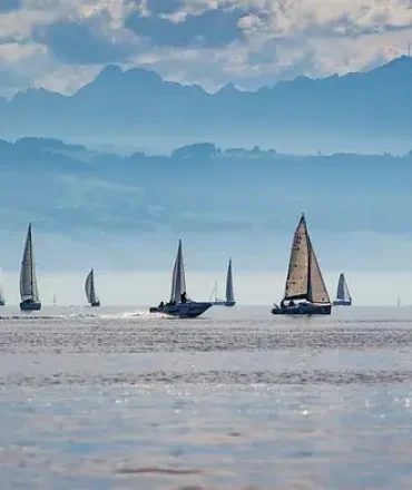 Segelboote auf dem Bodensee mit Alpenkulisse und leicht bewölktem Himmel