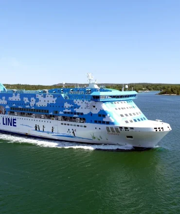 Große Fähre der Silja Line fährt durch das Meer vor finnischer Küste, bei Tageslicht mit Stadt und Bäumen im Hintergrund – Symbol für Skandinavien-Rundreisen.