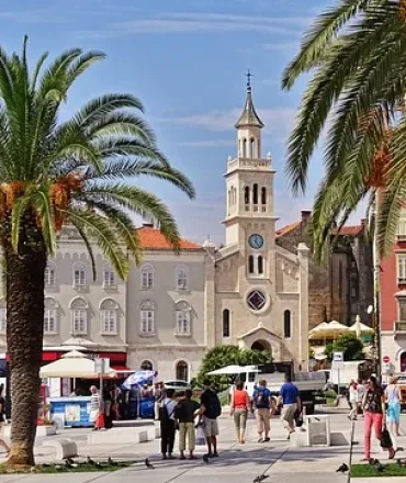 Platz mit Palmen und Cafés vor historischer Kirche in der Altstadt von Split, Kroatien