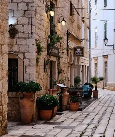Pflasterstraße mit Steinbauten, Laternen und Tavernen-Schild in kroatischer Altstadt mit mediterranem Flair