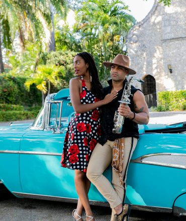 Urlaub Kuba. Mann und Frau stehen neben türkisfarbenem Oldtimer vor tropischer Kulisse – Symbol für stilvollen Roadtrip und Kuba-Erlebnis im Retro-Flair.