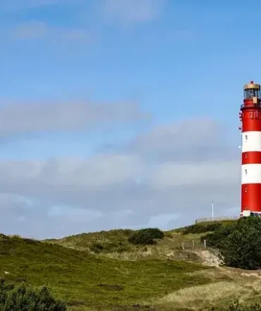 Rot-weißer Leuchtturm auf einer Düne auf Amrum unter blauem Himmel