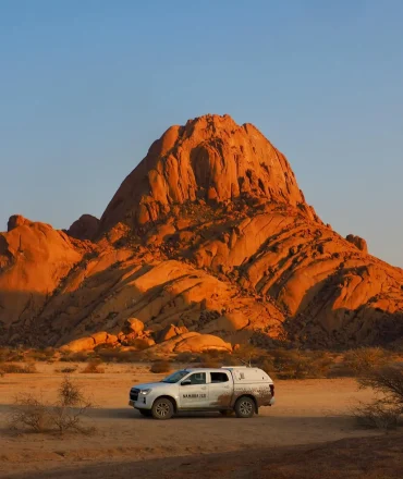 Namibia Urlaub. Offroad-Fahrzeug in der namibischen Wüste vor Felsformation – Abenteuerlandschaft in Namibia