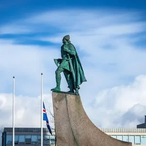 Reykjavik Statue in Reykjavik mit isländischer Flagge und moderner Architektur im Hintergrund