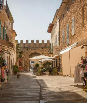 Charmante Straße in Alcúdia mit Steinbauten, Souvenirläden und historischem Tor bei Sonnenlicht
