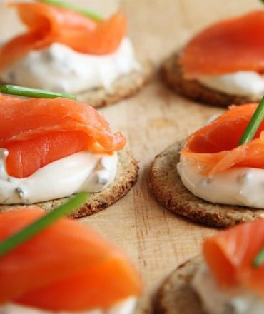 Skandinavien Urlaub. Mehrere Stücke Smørrebrød mit Räucherlachs und Frischkäse auf runden Crackern, appetitlich angerichtet auf hellem Untergrund – skandinavische Spezialität.