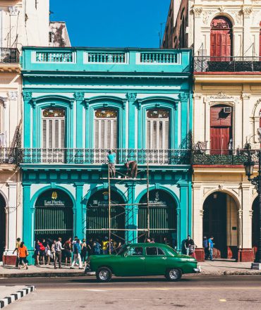 Hotel buchen. Pastellfarbene Kolonialgebäude und Oldtimer in Havanna – tropisches Straßenbild im historischen Zentrum von Kuba.