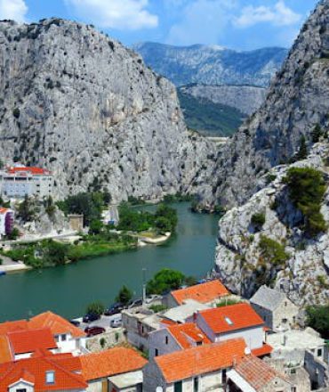 Kroatien Urlaub. Kroatische Stadt mit roten Dächern zwischen steilen Felsbergen und Fluss – Panoramaaufnahme mit mediterranem Flair