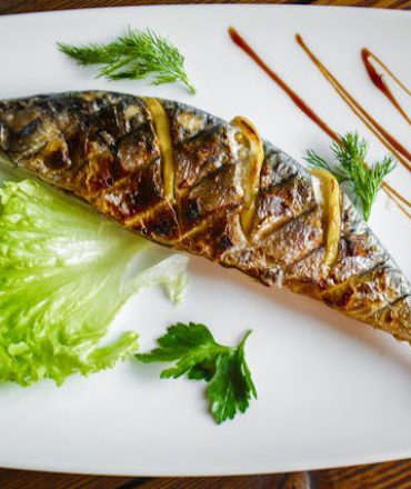 Gegrillter Fisch auf weißem Teller mit Kräutern, Salat und Sauce – mediterrane Küche in Kroatien