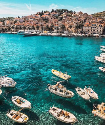 Urlaub Kroatien. Boote im türkisblauen Wasser vor mediterraner Küstenstadt mit roten Dächern und pastellfarbenen Häusern