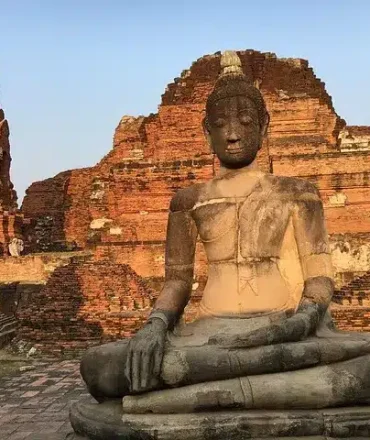Thailand Rundreise. Große Buddha-Statue vor antiken Backsteinruinen in Ayutthaya, Thailand – Symbol für historische und spirituelle Reiseziele abseits der Touristenpfade.