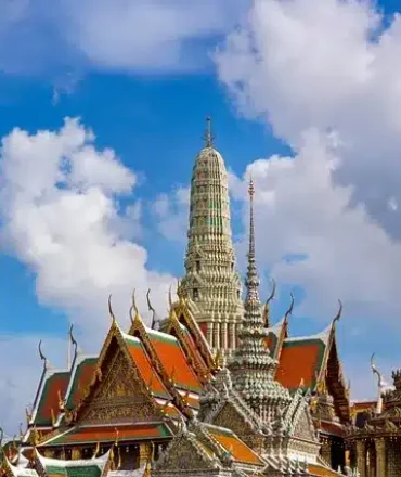 Thailand Urlaub. Prunkvolle Tempel in Bangkok mit goldenen Spitztürmen und kunstvollen Fassaden vor blauem Himmel – typisch für Thailands kulturelles Erbe.