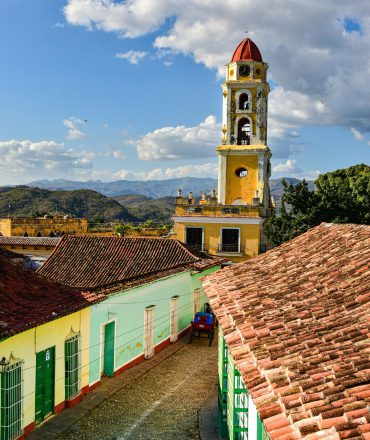 Urlaub Kuba. Kopfsteinpflasterstraße mit bunten Kolonialhäusern und gelbem Glockenturm in Trinidad, Kuba – Symbol für karibische Lebensfreude und historische Architektur.